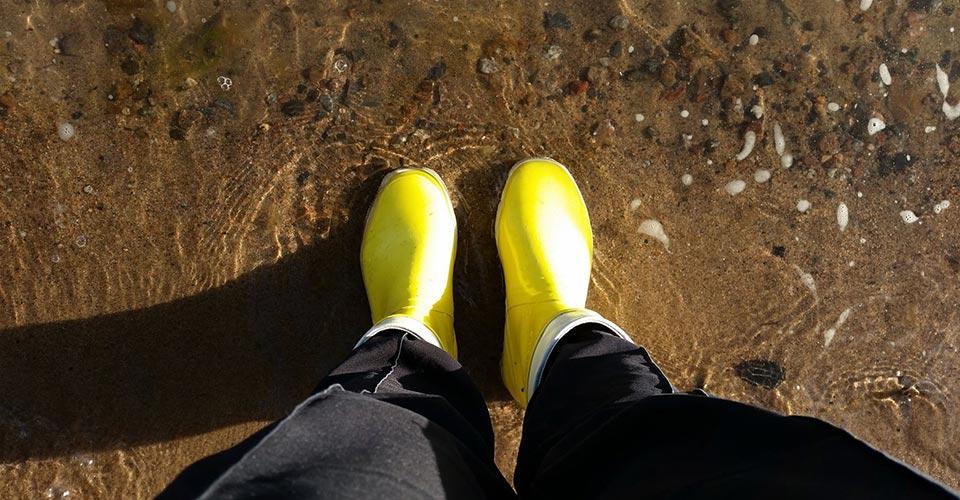 Henkilö seisoo keltaiset kumisaappaat jalassa rantavedessä.