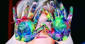 Lapsen moniväriset maaliset kädet kasvojen edessä