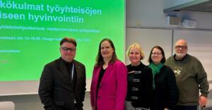 Viisi henkilöä seisovan tekstiesityksen edessä.