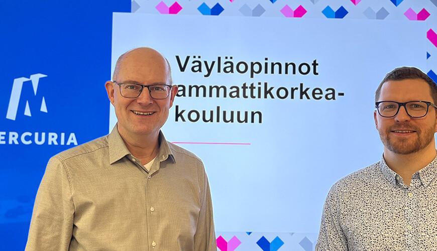Kaksi henkilöä seisoo ilmoituksen edessä, jossa lukee: Väyläopinnot ammattikorkeakouluun.