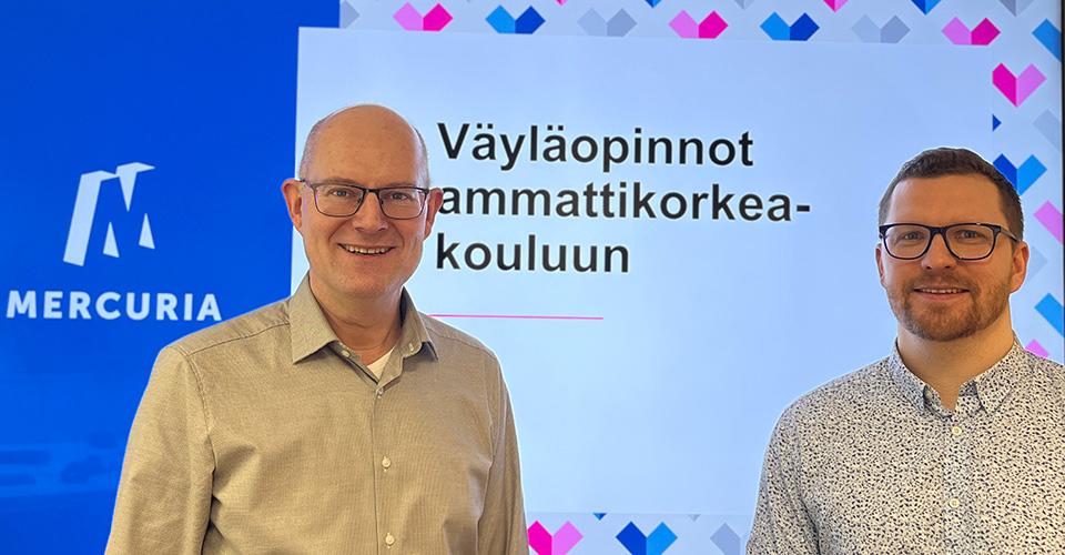 Kaksi henkilöä seisoo ilmoituksen edessä, jossa lukee: Väyläopinnot ammattikorkeakouluun.