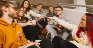 Nuoria istuu portailla ja katselee kahden henkilön etusormia.