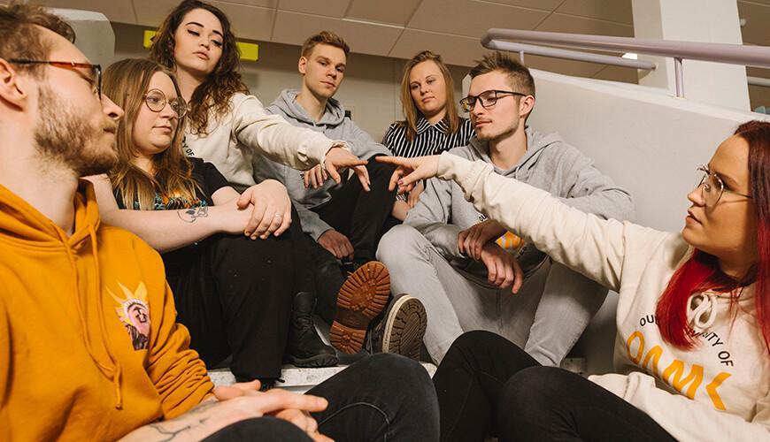 Nuoria istuu portailla ja katselee kahden henkilön etusormia.